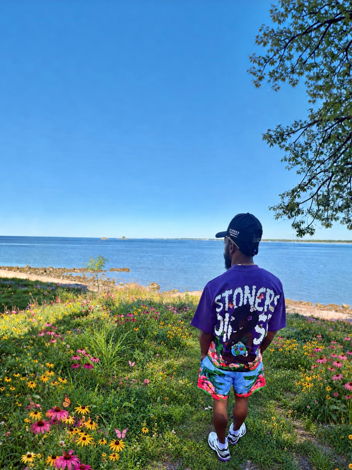 Purple Gaia tee and floral shorts beside the water